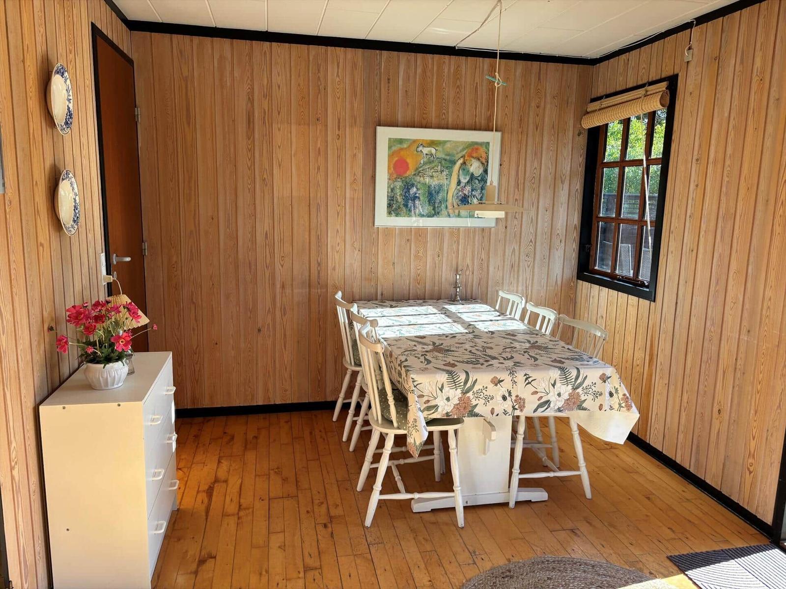 Dining room with wood paneling, table with chairs and window.