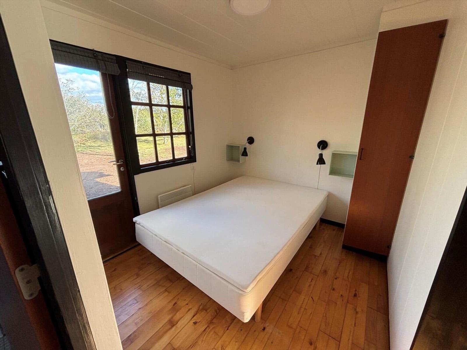 Bedroom with bed, window, and wooden floor.