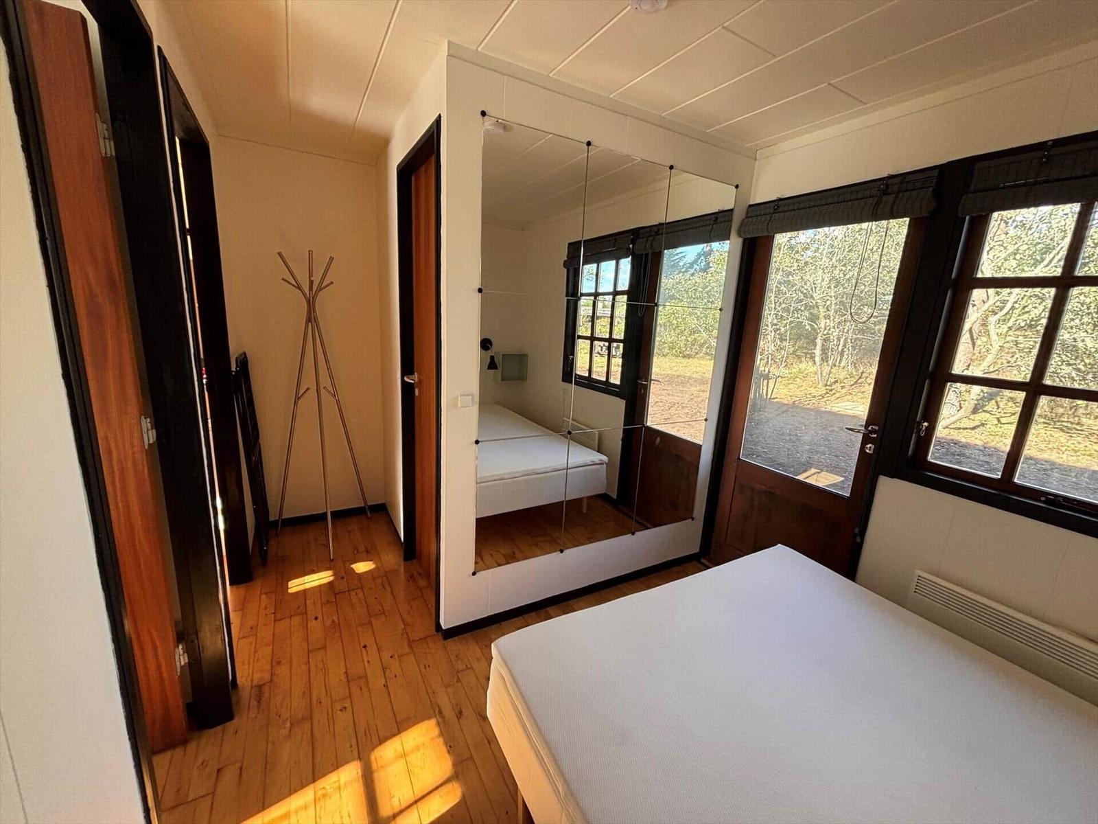 Bedroom with wooden floor, mirrored wall, and windows to the garden