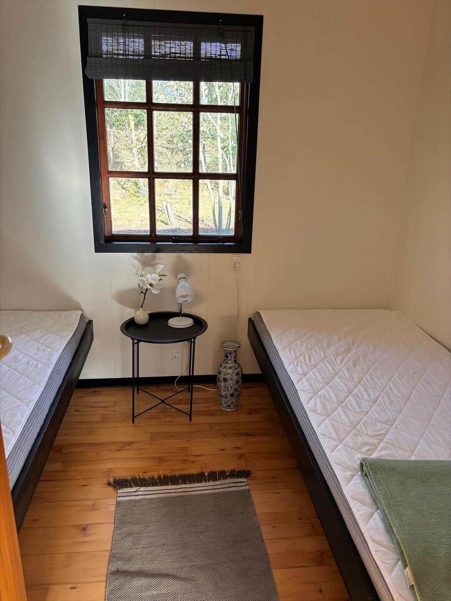 Two sleeping areas with mattresses, small table, and window with view of forest.