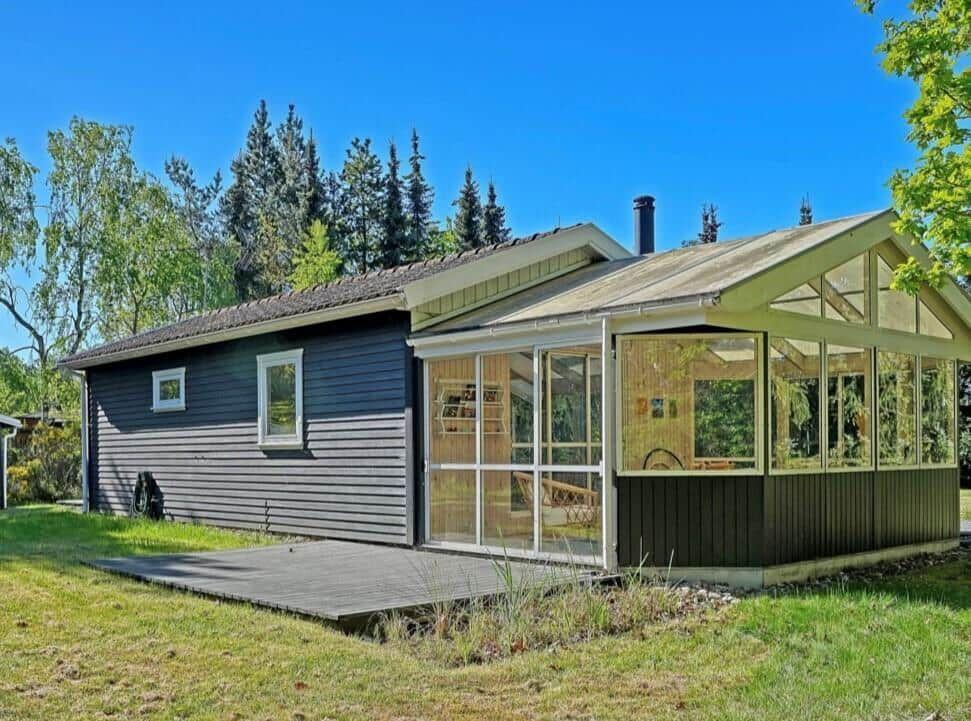 Modern cabin with glass porch and wood siding in a green setting.