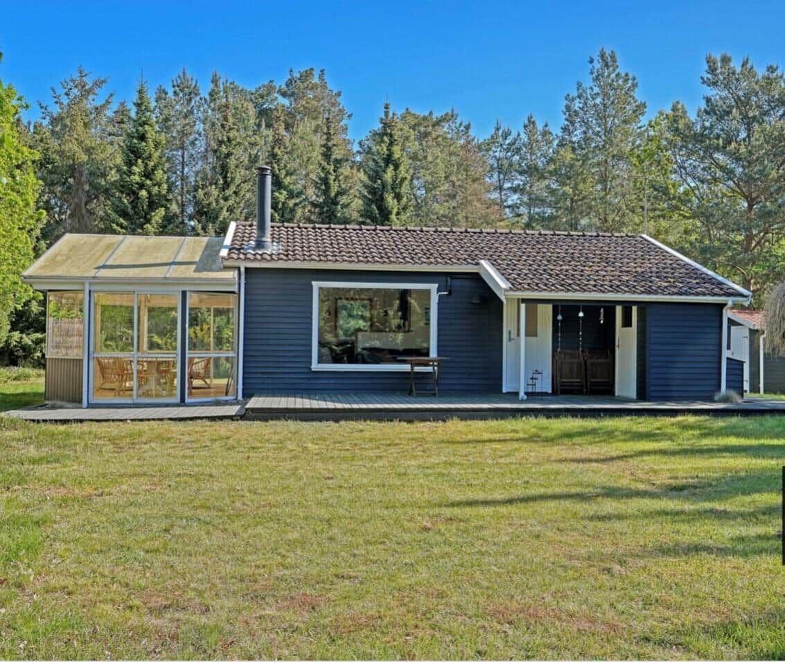 A dark blue wooden house with a terrace and glass veranda in the green.
