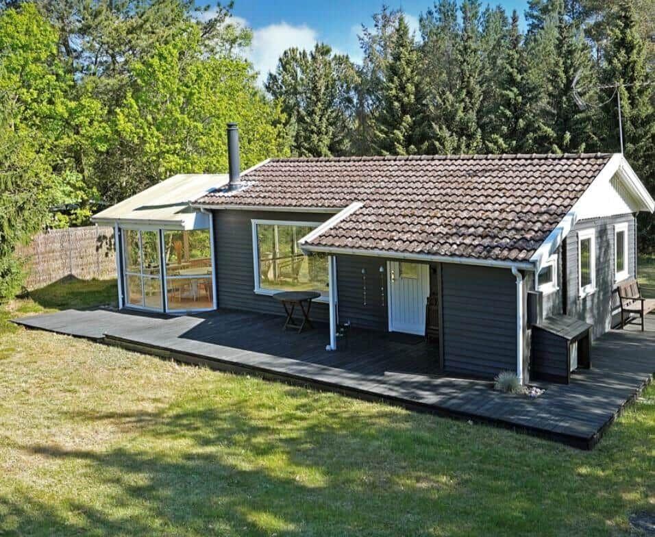 A house with wooden deck, glass enclosure, and tiled roof surrounded by trees.
