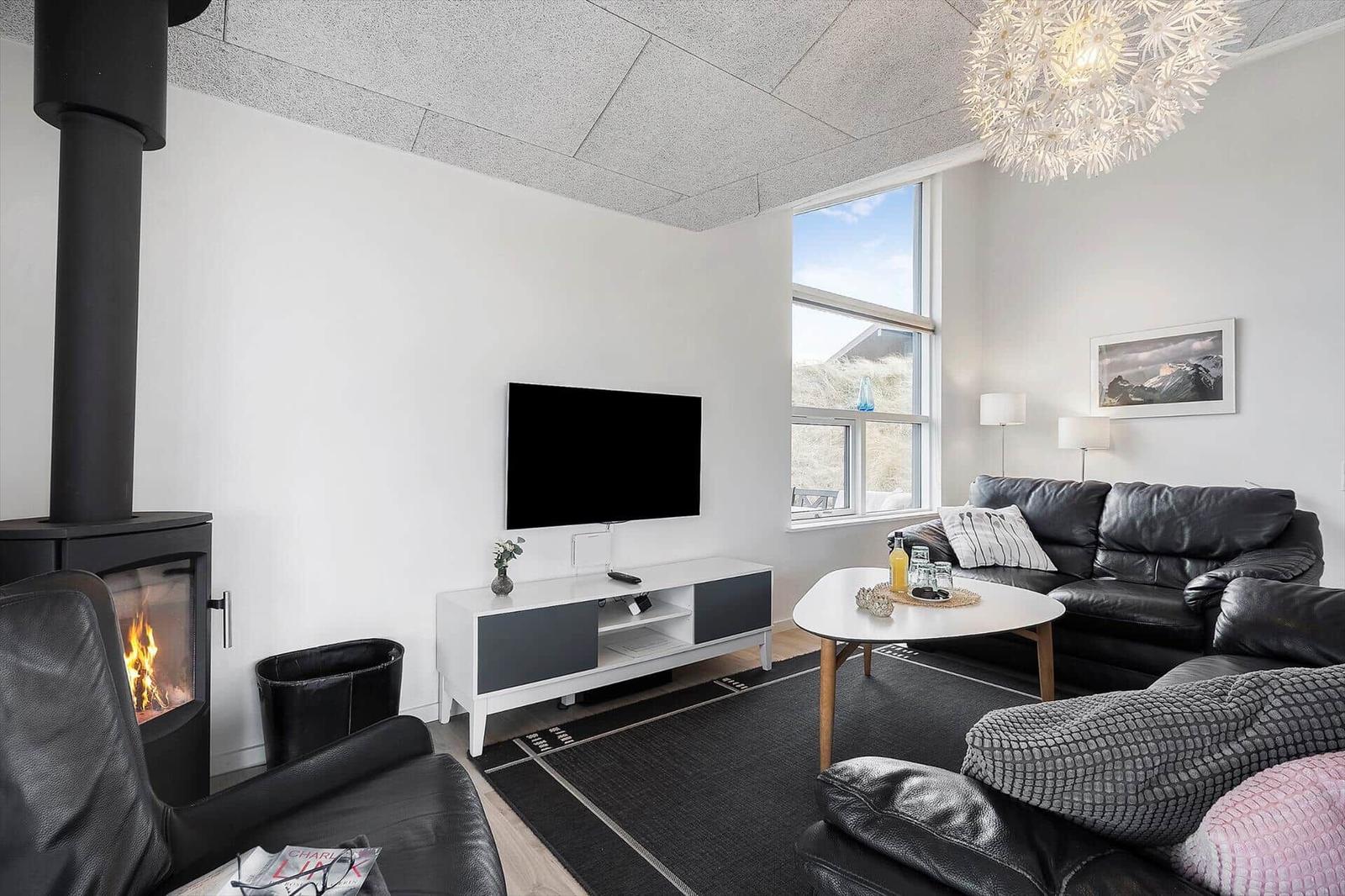 Wohnzimmer mit Kamin, Sofa, TV und großem Fenster.