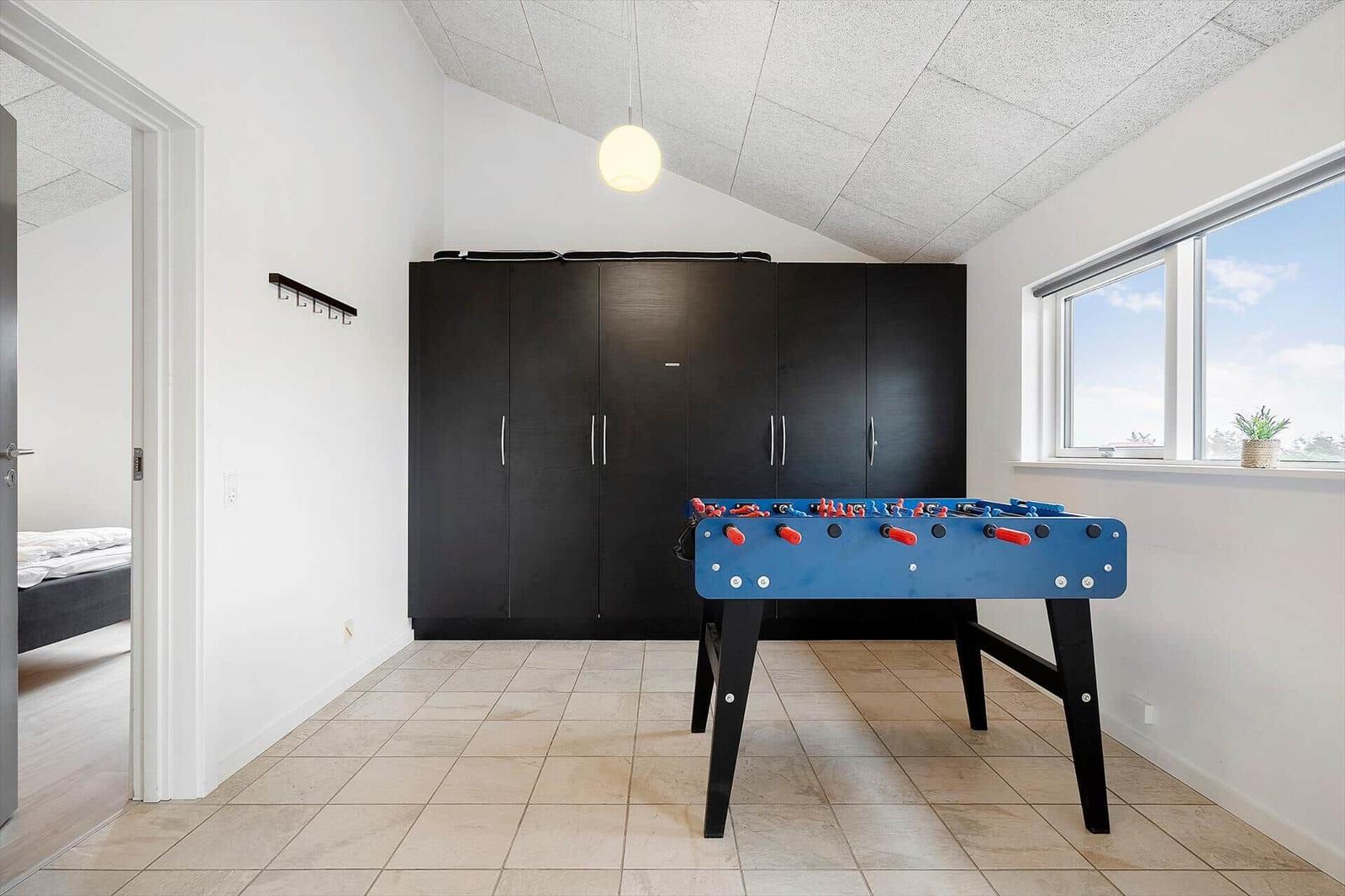 Raum mit Fußballecke, schwarzen Schränken und Fenster. Tür führt in Schlafzimmer.