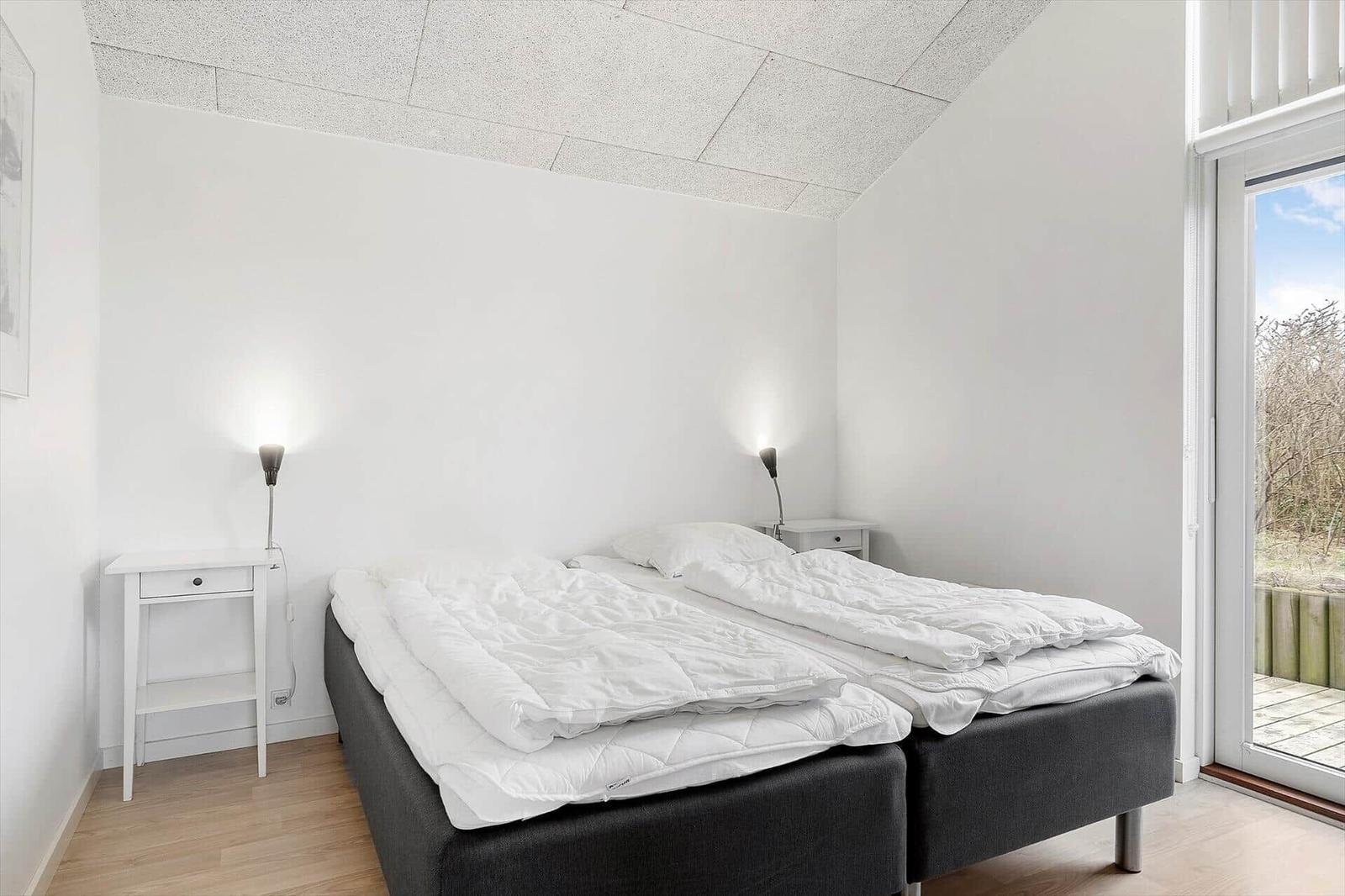 Schlafzimmer mit Doppelbett, zwei Nachttischen und Fenster zur Terrasse.