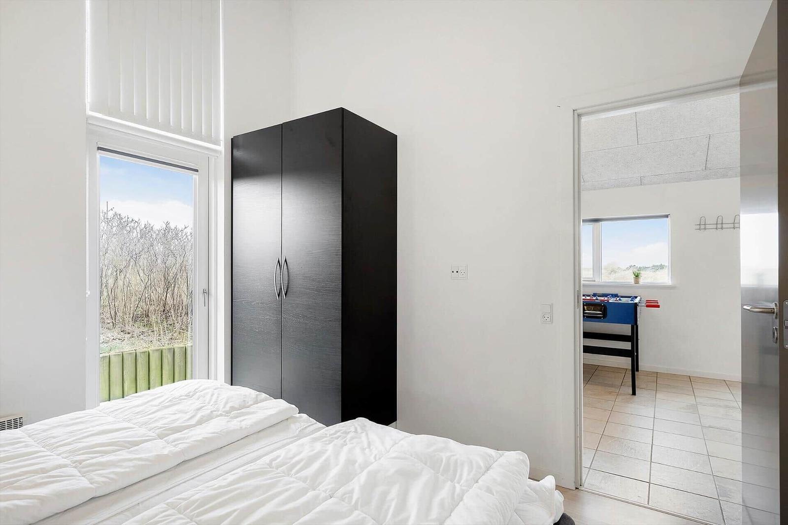 Schlafzimmer mit Bett, Kleiderschrank und Fenster. Durchgang zu einem Raum mit Tischfußball.