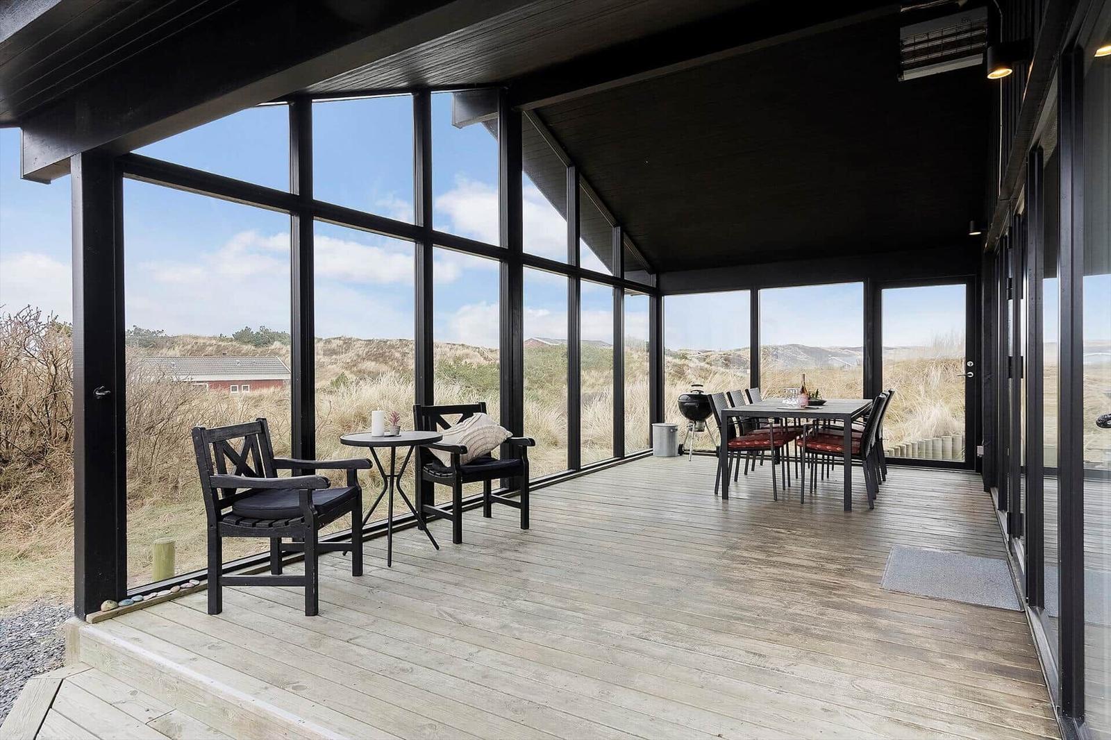 Terrasse mit Sitzgelegenheiten und Grill, Blick auf Dünenlandschaft.
