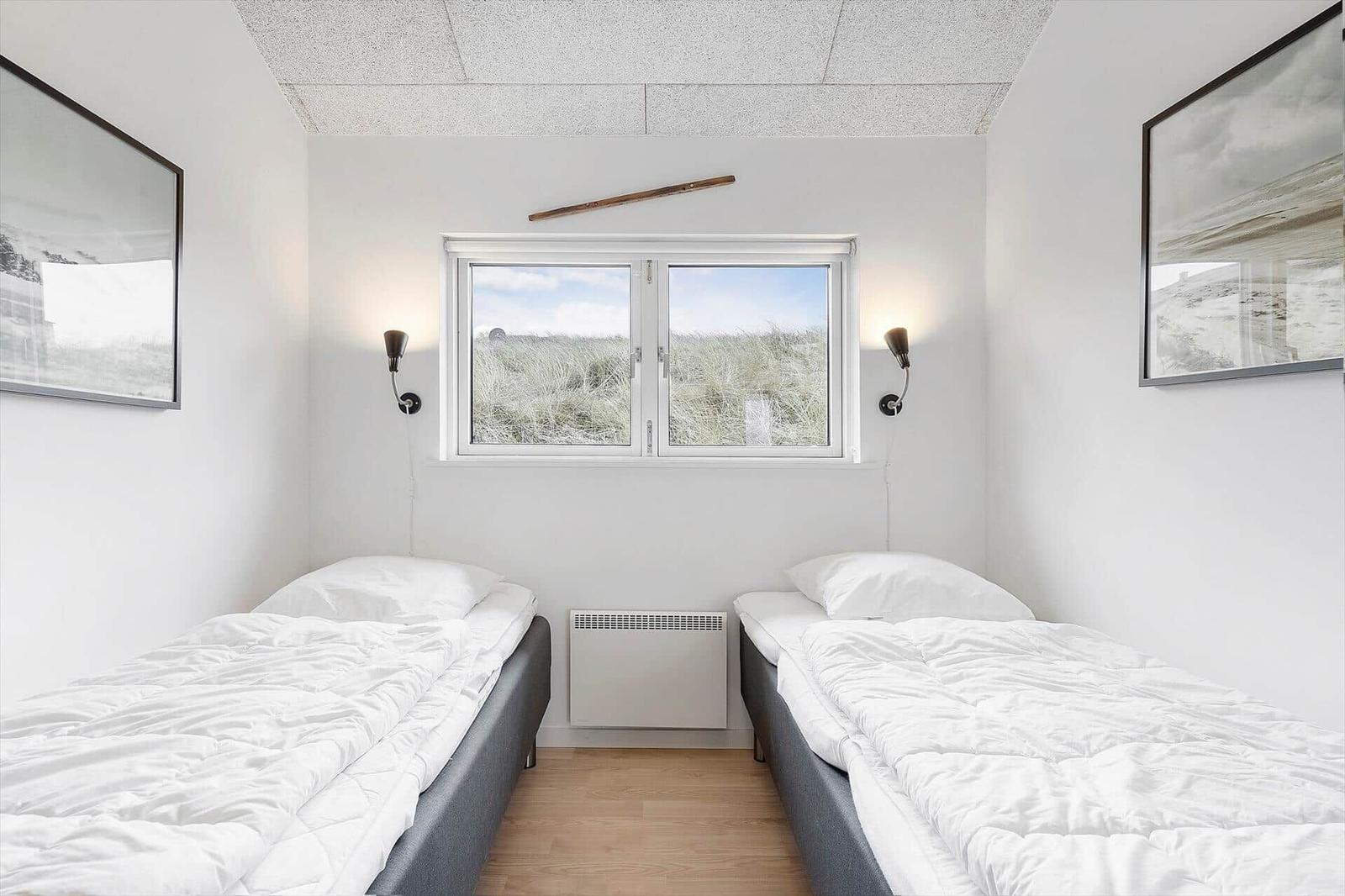 Zwei Betten mit weißen Laken, Fenster mit Strandblick und Wandlampen.