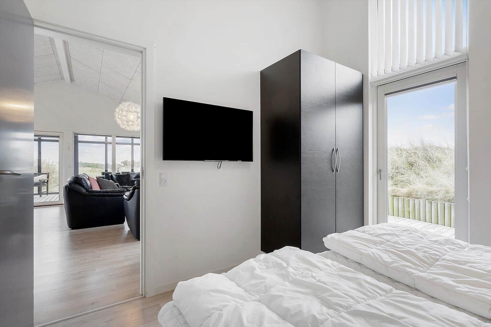 Schlafzimmer mit Bett, Kleiderschrank und Fernseher. Durchgang zum Wohnzimmer mit Sitzgelegenheit.