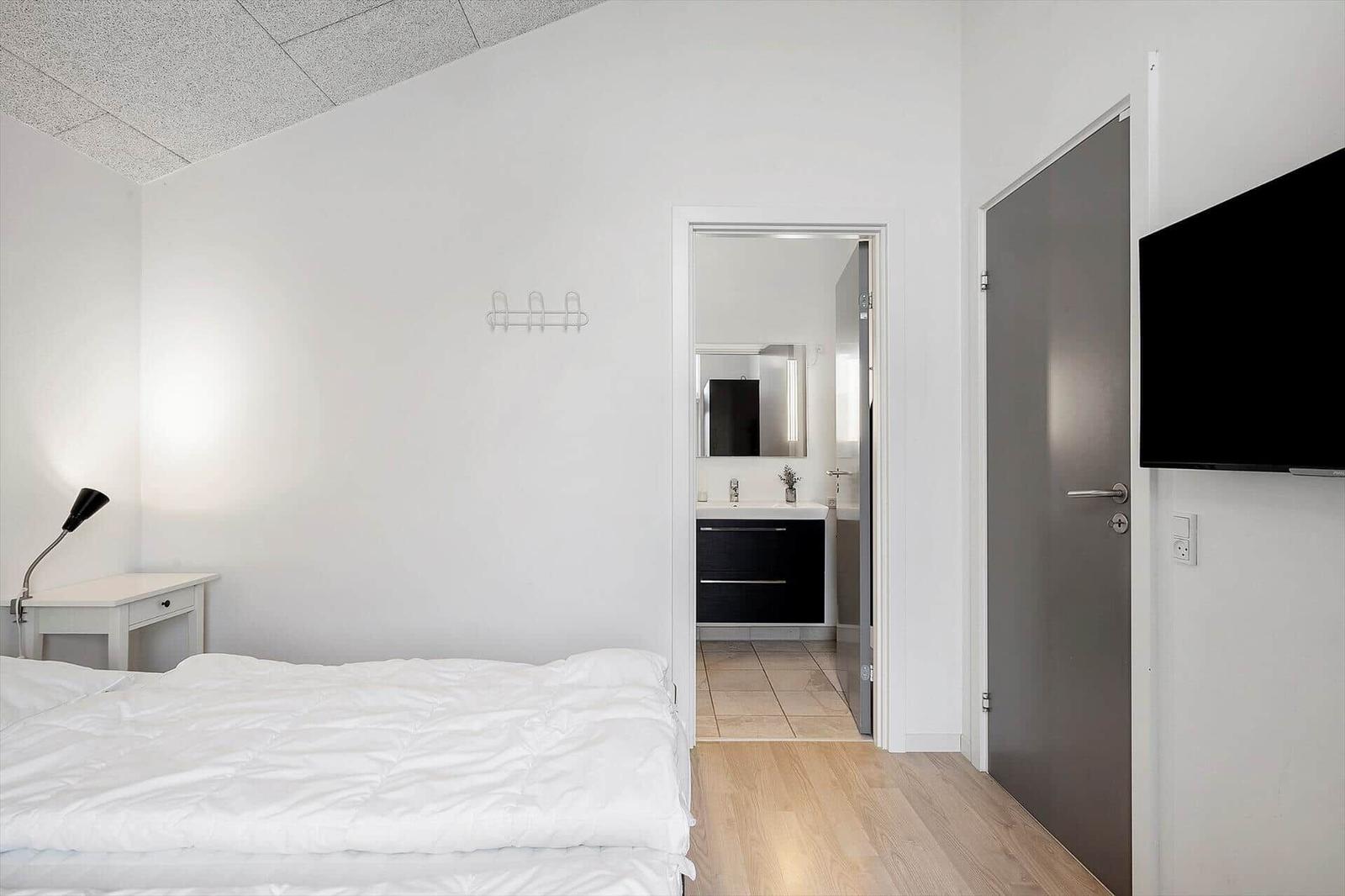 Schlafzimmer mit Bett, Schreibtisch und TV. Tür führt zum Badezimmer.