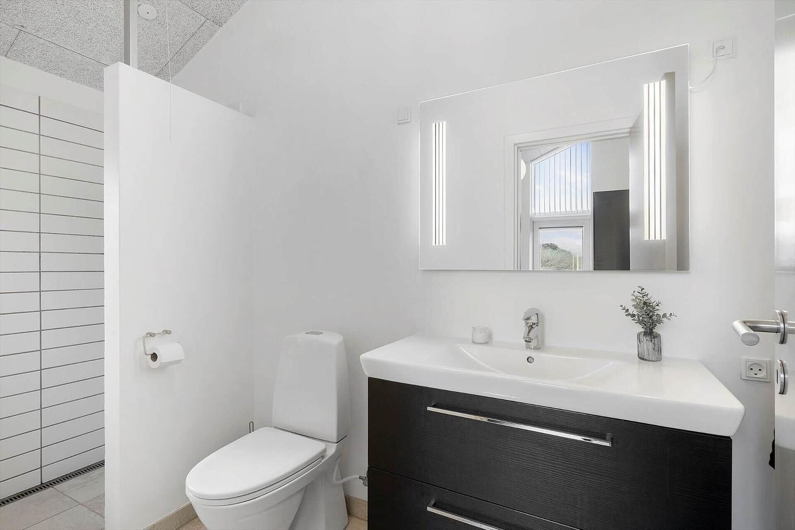 Badezimmer mit Toilette, Waschbecken und Spiegel mit Beleuchtung.