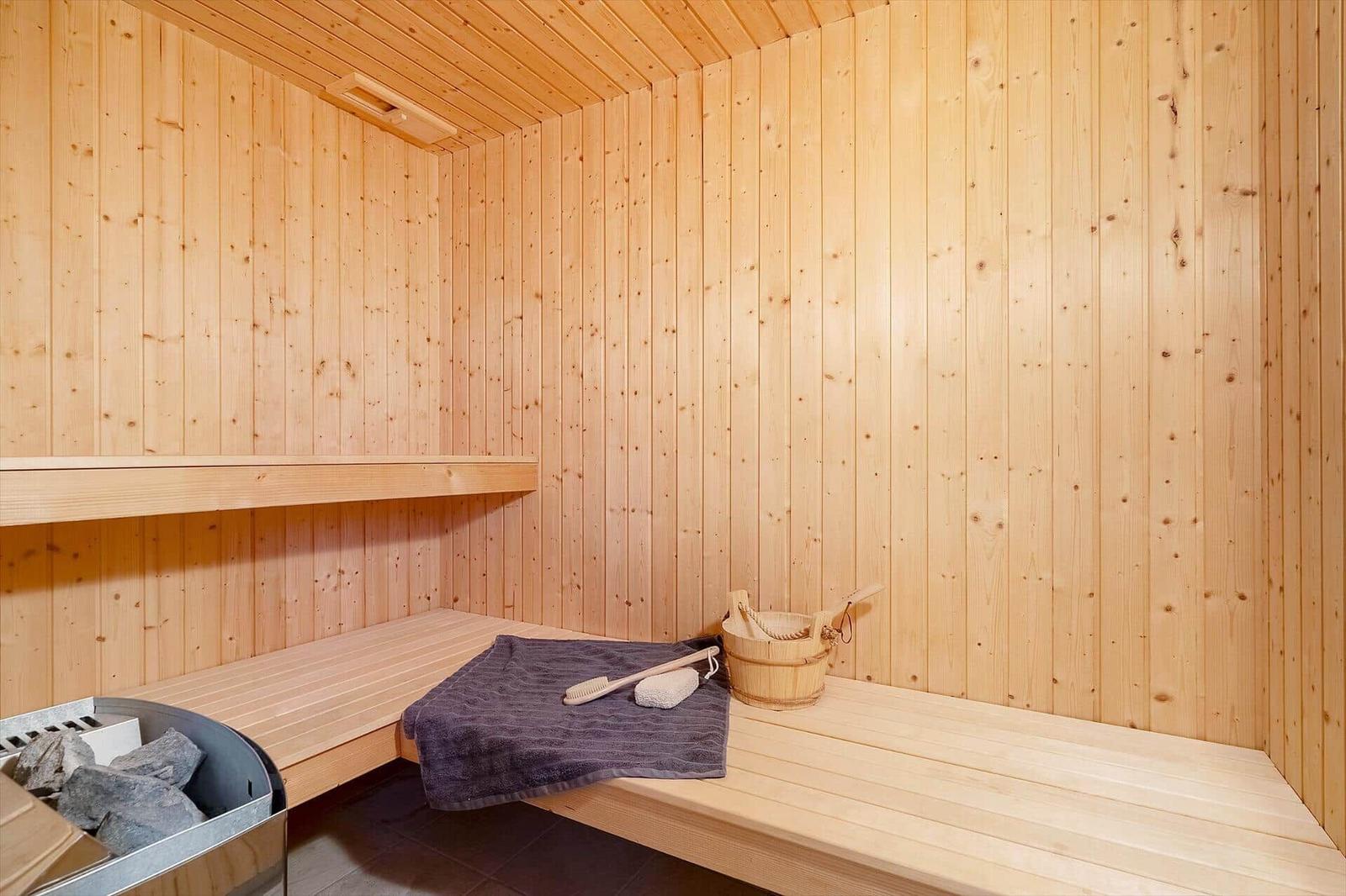Sauna mit Holzbank, Holzwand und Holzdecke. Dampfstein, Eimer und Handtuch sind vorhanden.