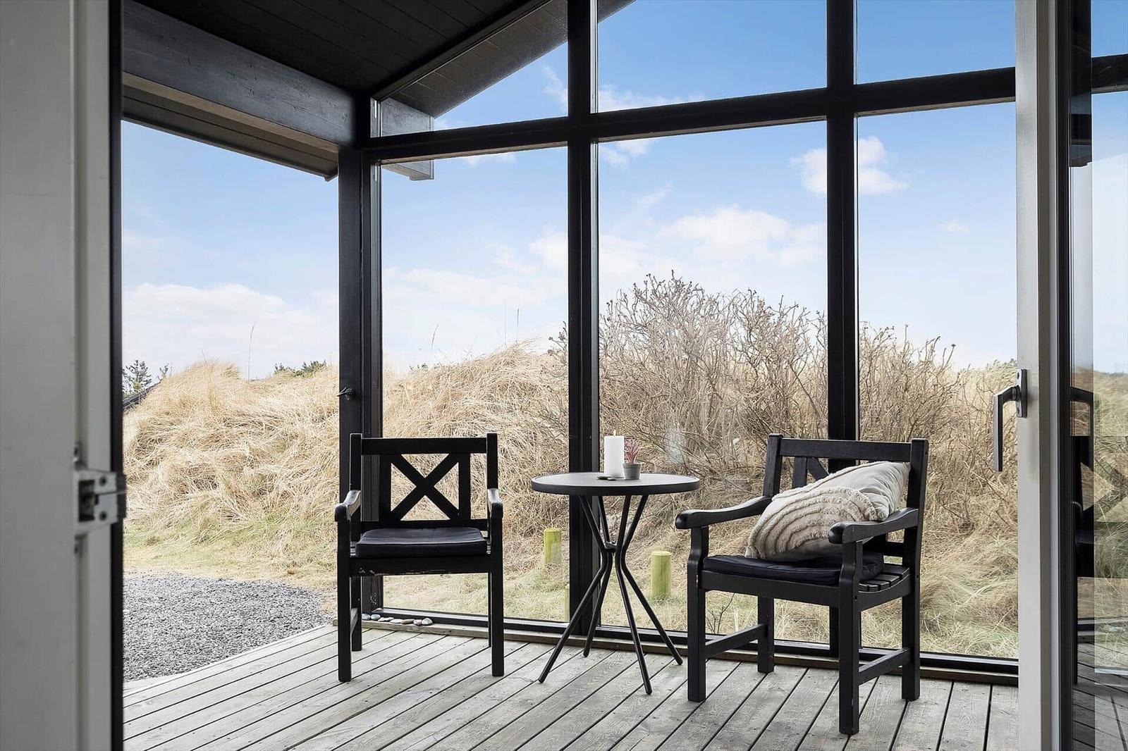 Terrasse mit zwei Stühlen und Tisch. Blick auf Dünen und Himmel.