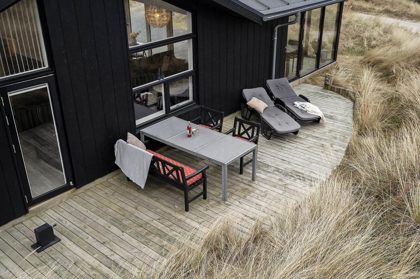 Terrasse mit Tisch, Stühlen und Liegen neben schwarzem Haus
