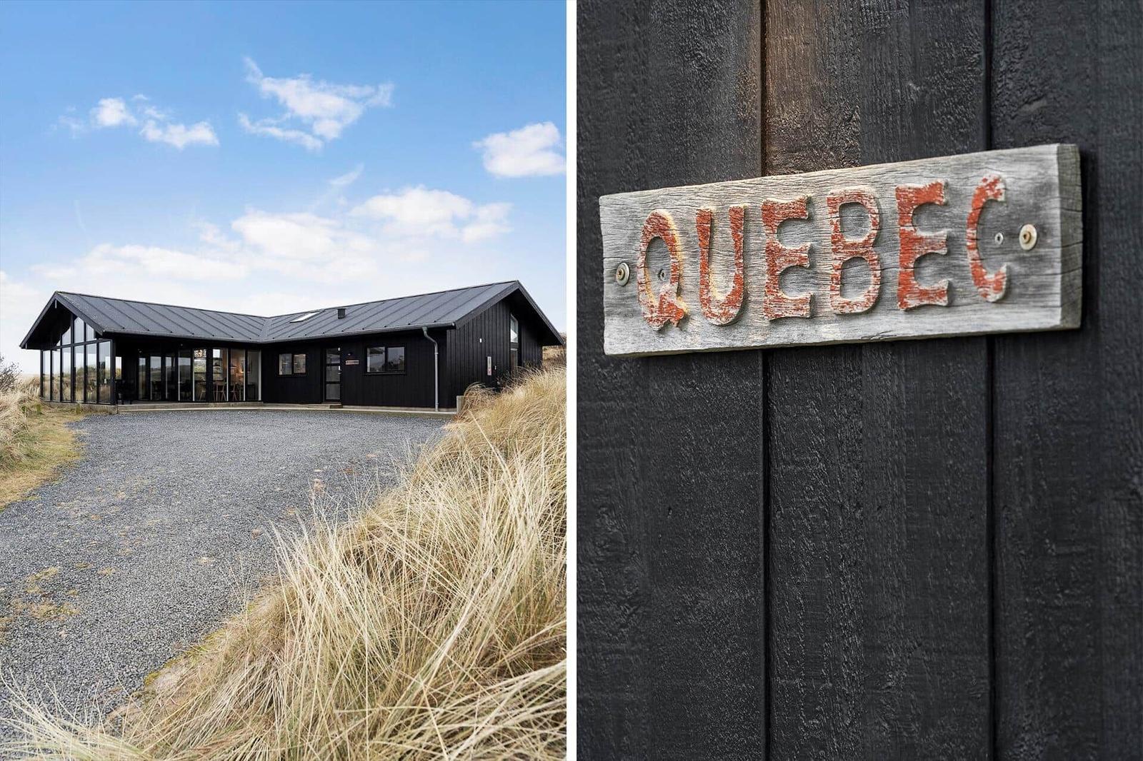 Modernes Haus mit Holzverkleidung und großem Fensterbereich. Holzschild mit Aufschrift Quebec.