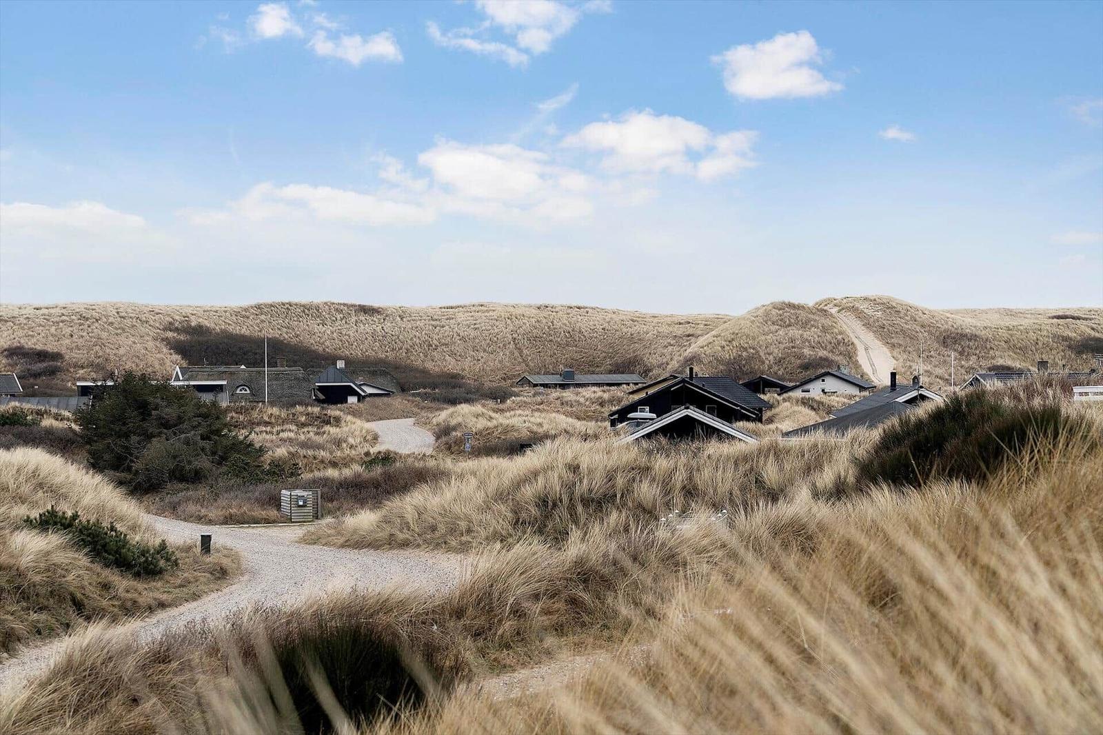 Häuser unter sanddünen mit steinweg und blauem himmel.