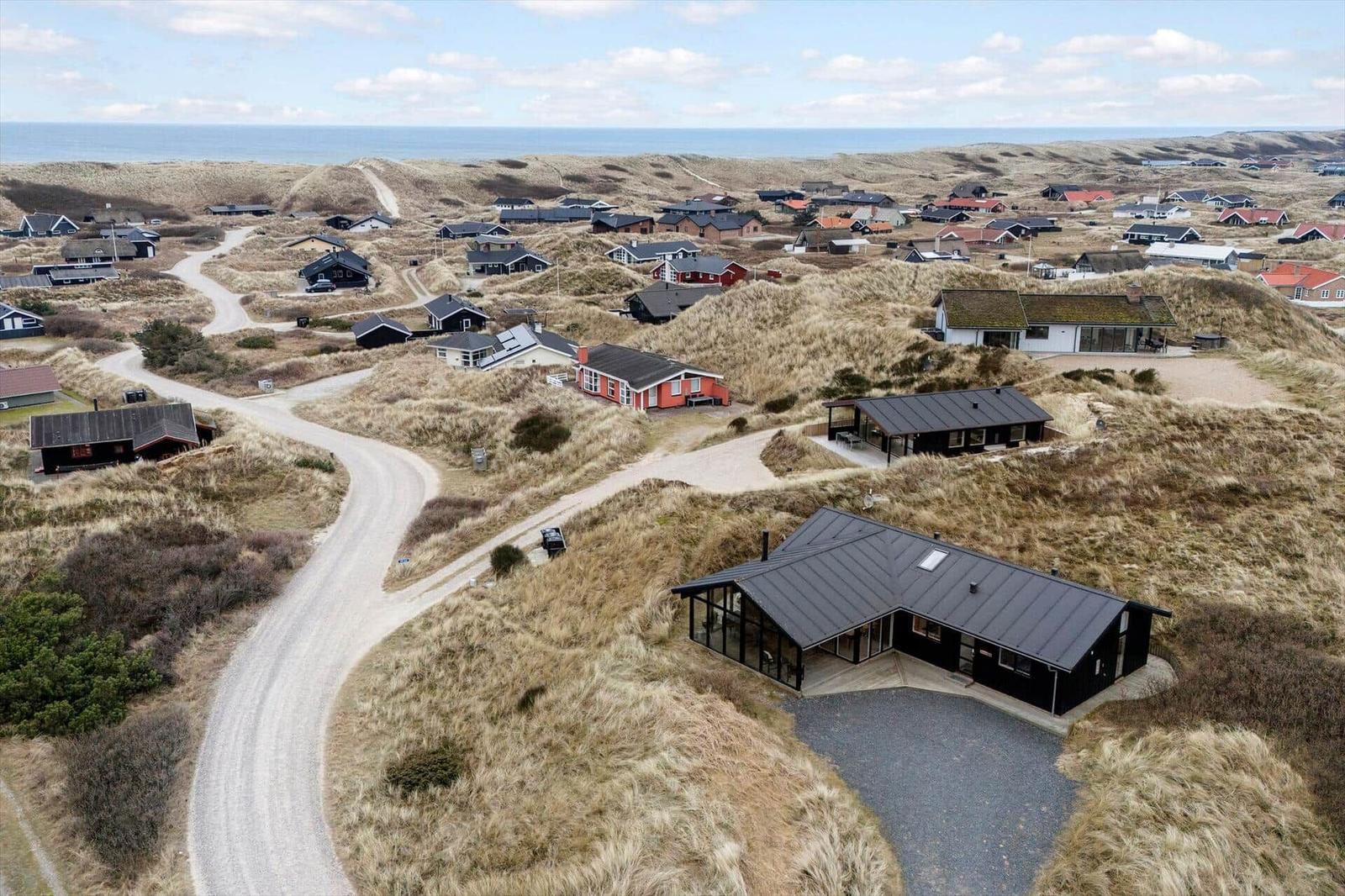 Modernes Haus auf Dünen mit Blick aufs Meer und kleinem Dorf.