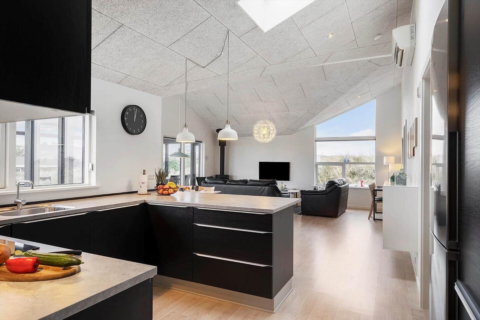 Moderne Küche mit Kücheninsel und Blick in Wohnzimmer mit Sofa und TV.