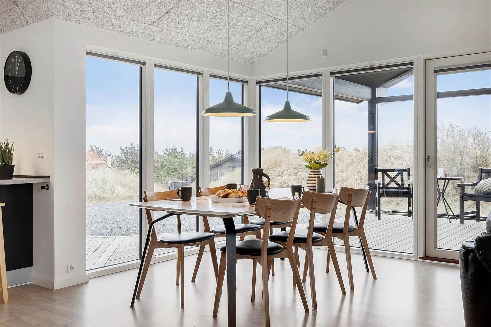 Esszimmer mit Tisch, Stühlen und großen Fenstern zur Terrasse.