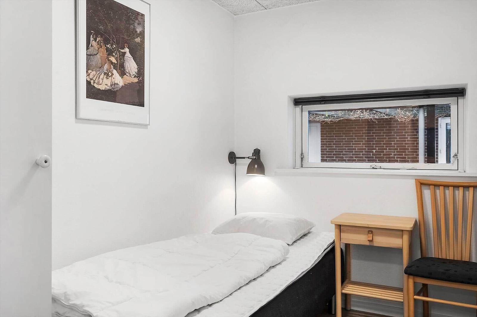 Ein Schlafzimmer mit Bett, Stuhl und Tisch. An der Wand hängt ein Bild.