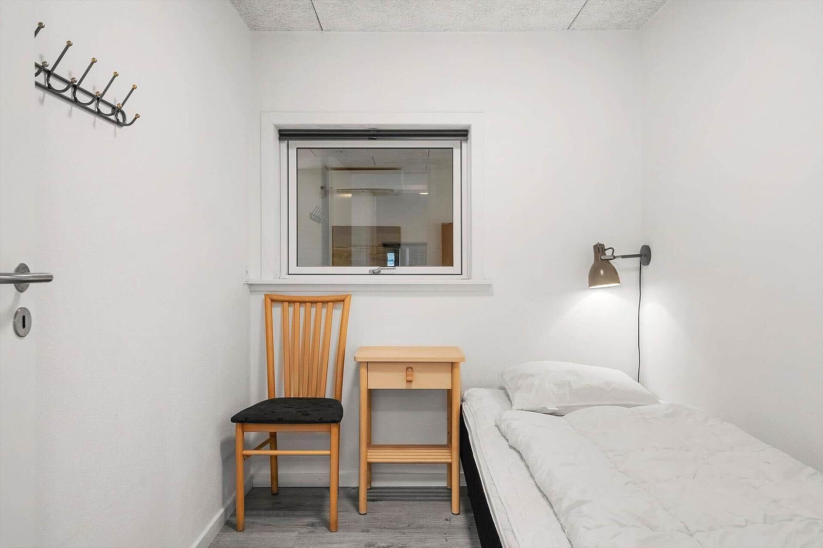 Ein Schlafzimmer mit Bett, Stuhl und Nachttisch. An der Wand hängt eine Lampe.