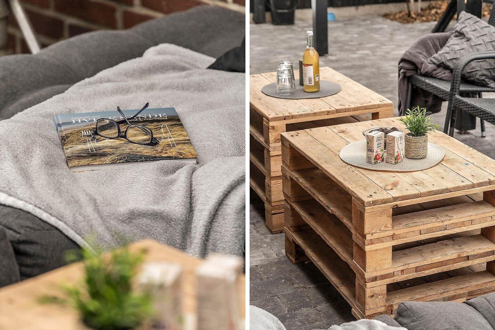 Außenbereich mit Holztischen und grauen Sitzmöbeln. Auf einem Tisch steht eine Flasche und zwei Gläser.