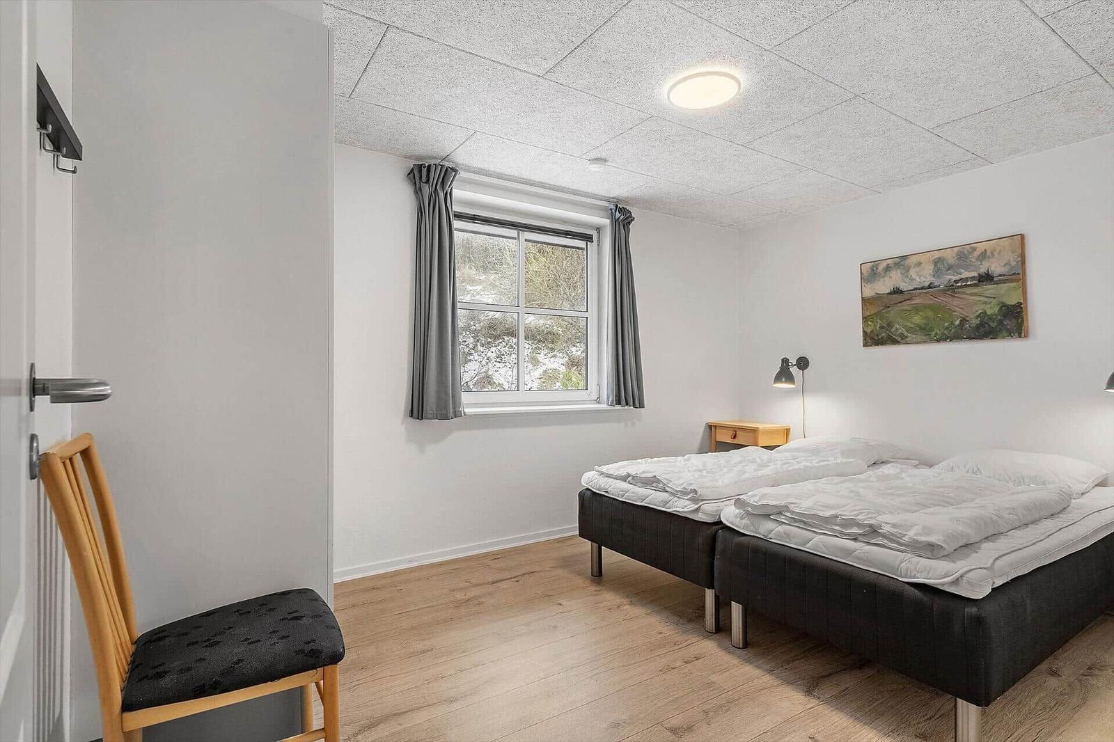 Zwei Schlafplätze, Fenster mit grauen Vorhängen, Holzboden und Wandbild.