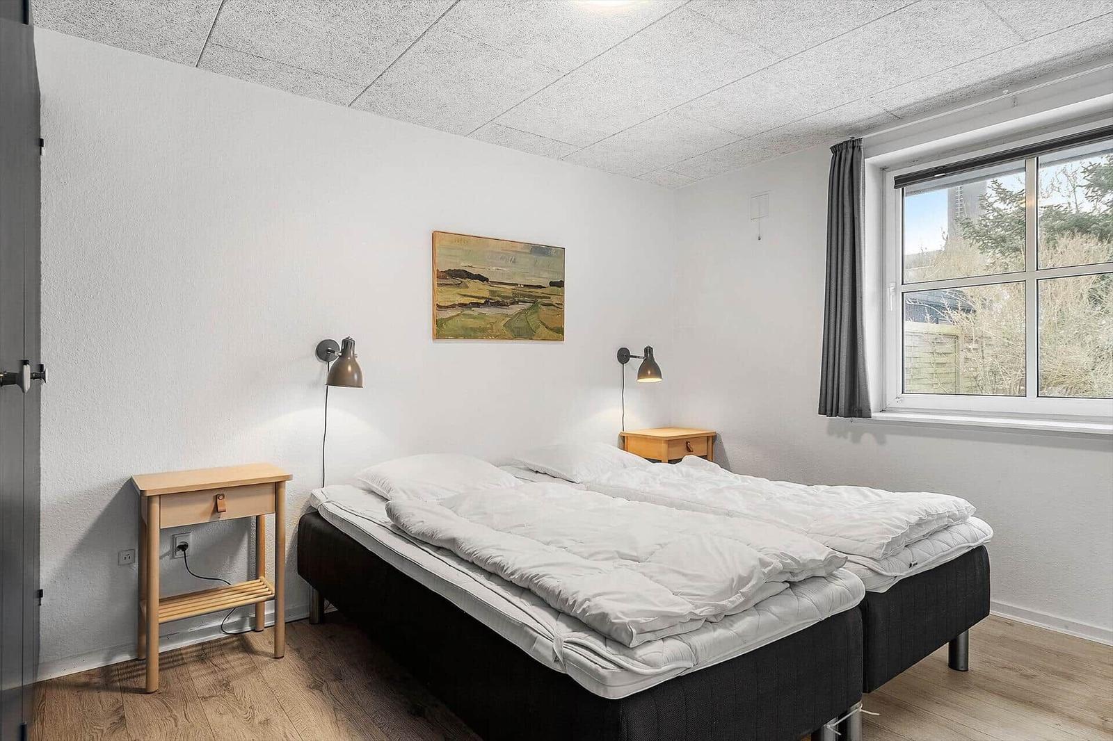 Schlafzimmer mit Doppelbett, zwei Nachttischen und Fenster.