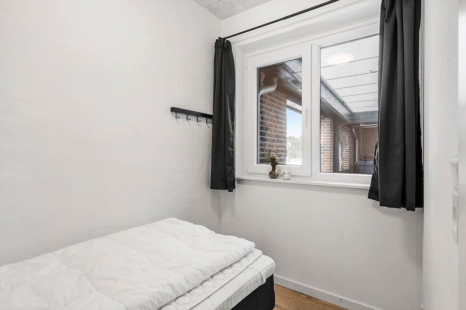 Schlafzimmer mit Bett, Fenster und Gardinen.