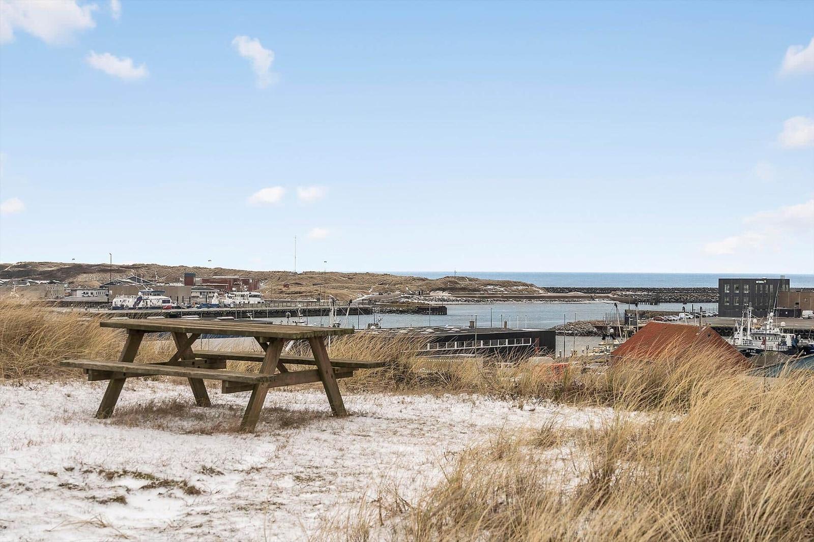 Holztisch auf sandigem Boden mit Blick auf Hafen und Meer.
