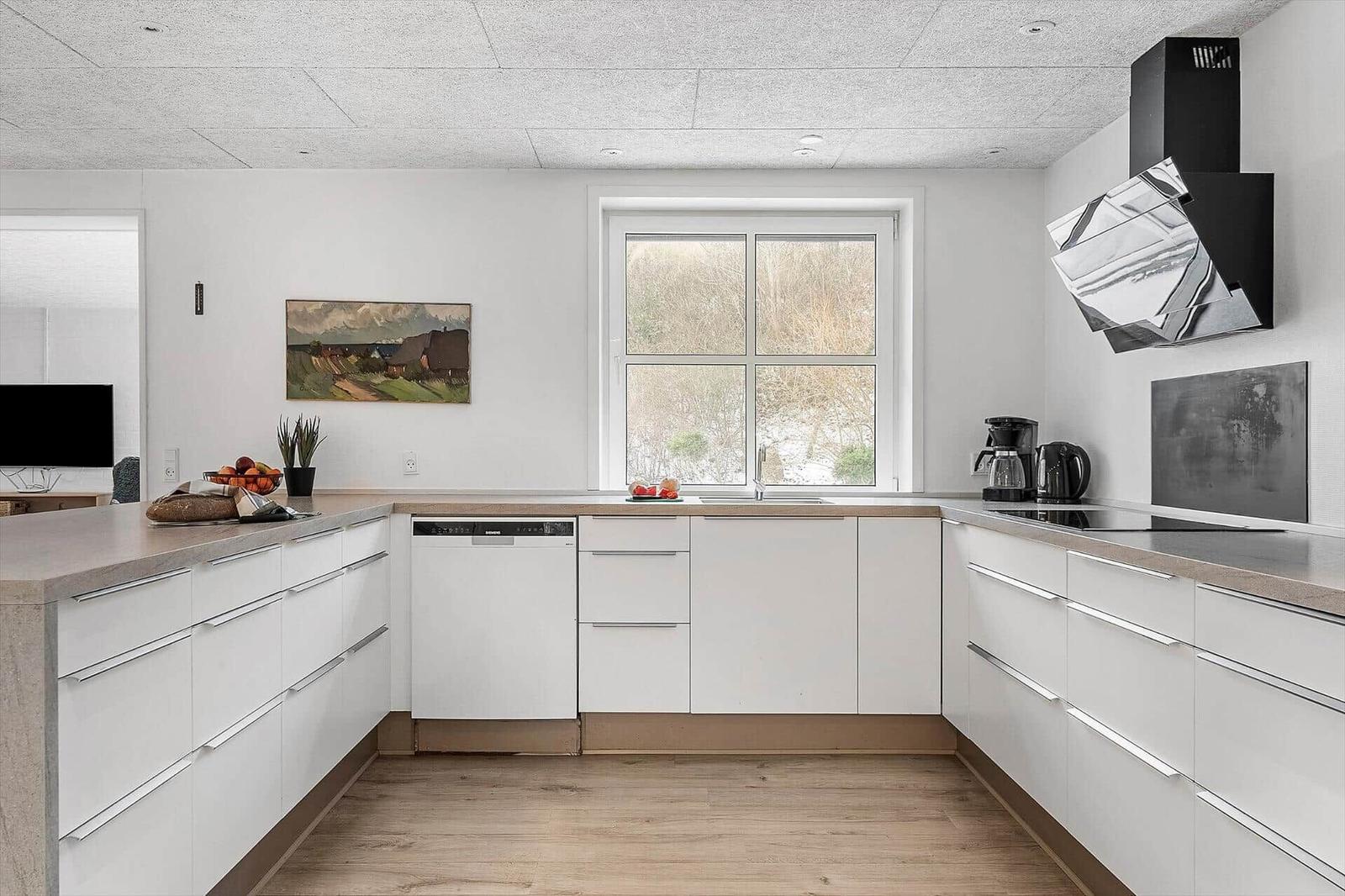 Moderne Küche mit weißer Einbauküche, Holzboden und Fensterblick.