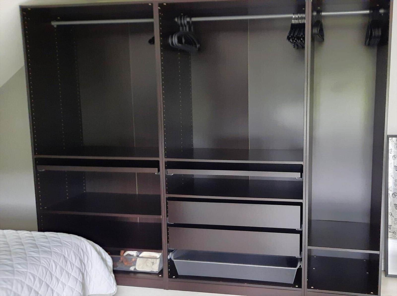 Großer Kleiderschrank mit Haken, Regalen und Schubladen. Bett ist teilweise sichtbar.