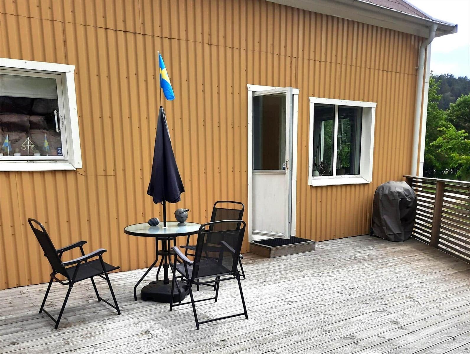Terrasse mit Tisch, Stühlen und schwedischer Flagge vor einem Haus mit Wellblechfassade.