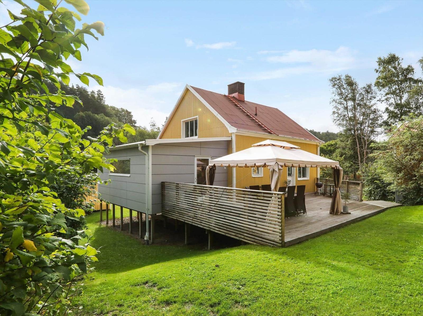 Haus mit Terrasse, Sonnenschutz und Garten. Umgeben von Bäumen und Gras.