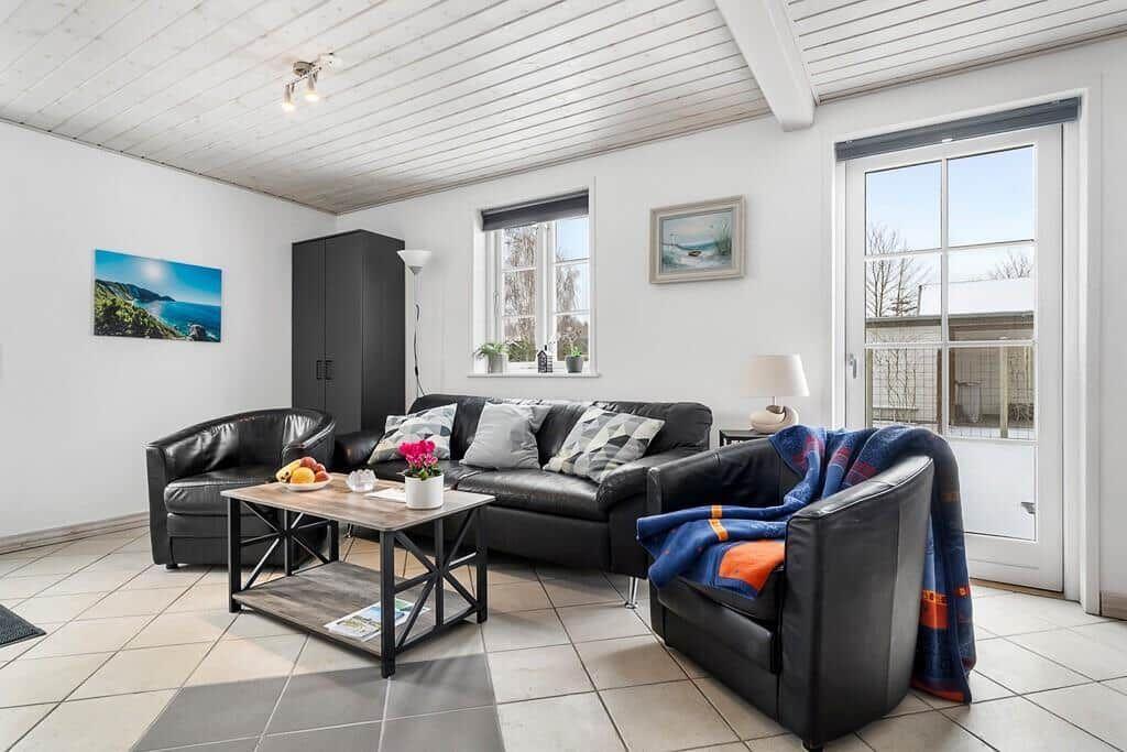 Living room with black leather furniture, wooden table, and windows.