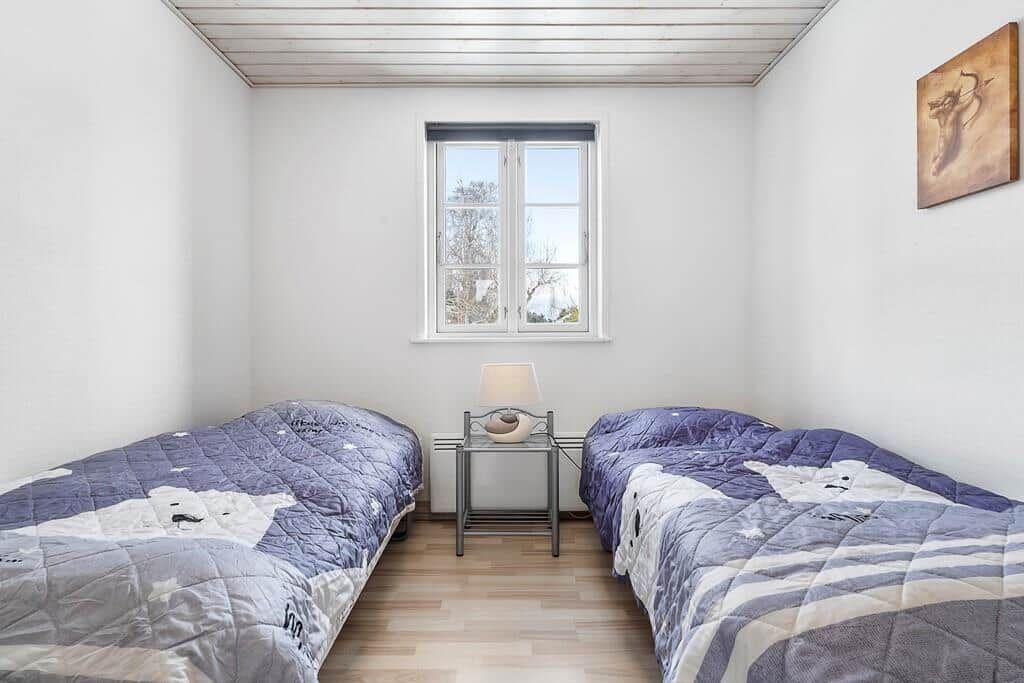 Two single beds with patterned bedspreads, a window, and a lamp.