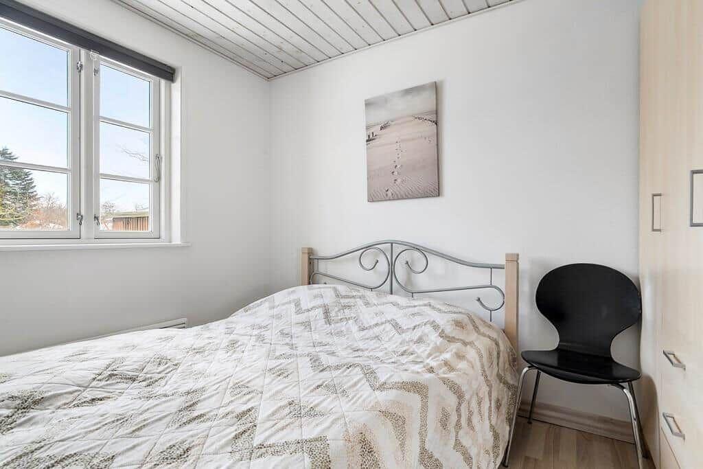 Bedroom with bed, window, and chair. Wall art and wooden floor.