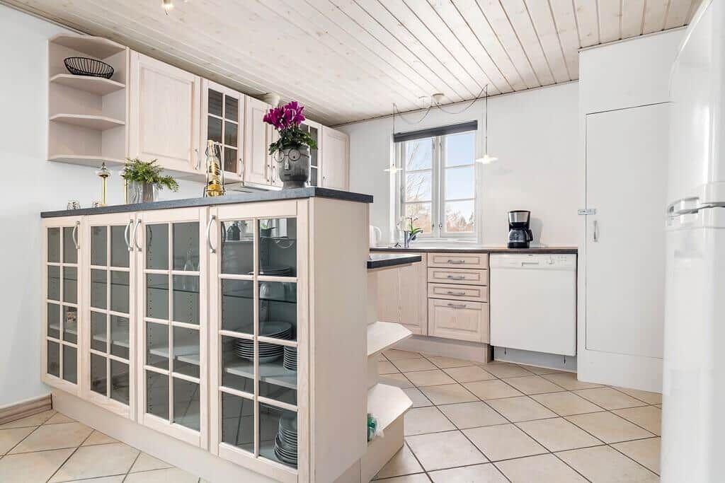 Kitchen with light cabinets, glass fronts, and tiled floor. Window and ceiling visible.