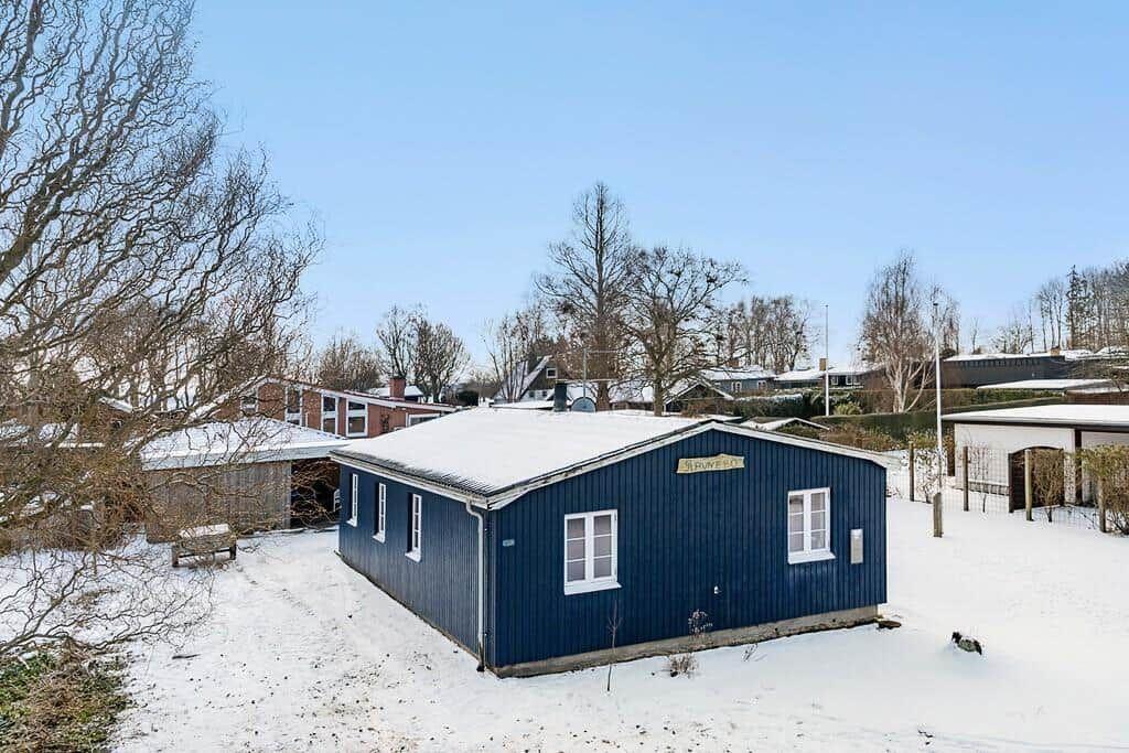 Blue wooden shed covered in snow, surrounded by trees and other buildings.