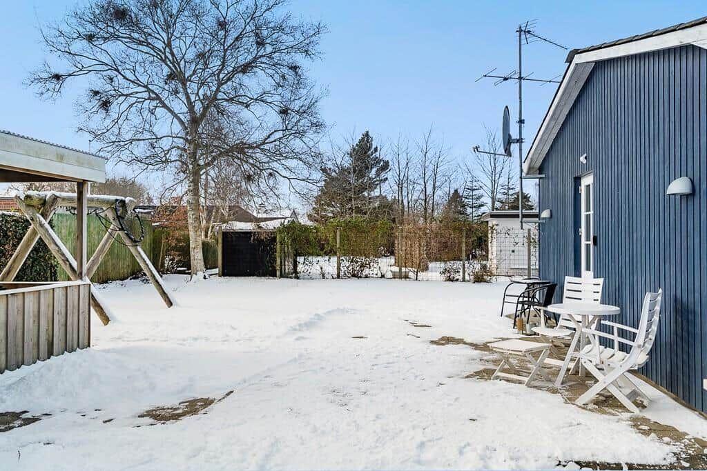 Snow-covered garden with blue house and white table set.
