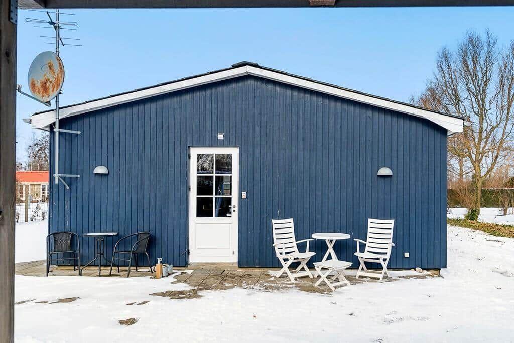 Blue wooden house with white door and outdoor table with chairs in snow.
