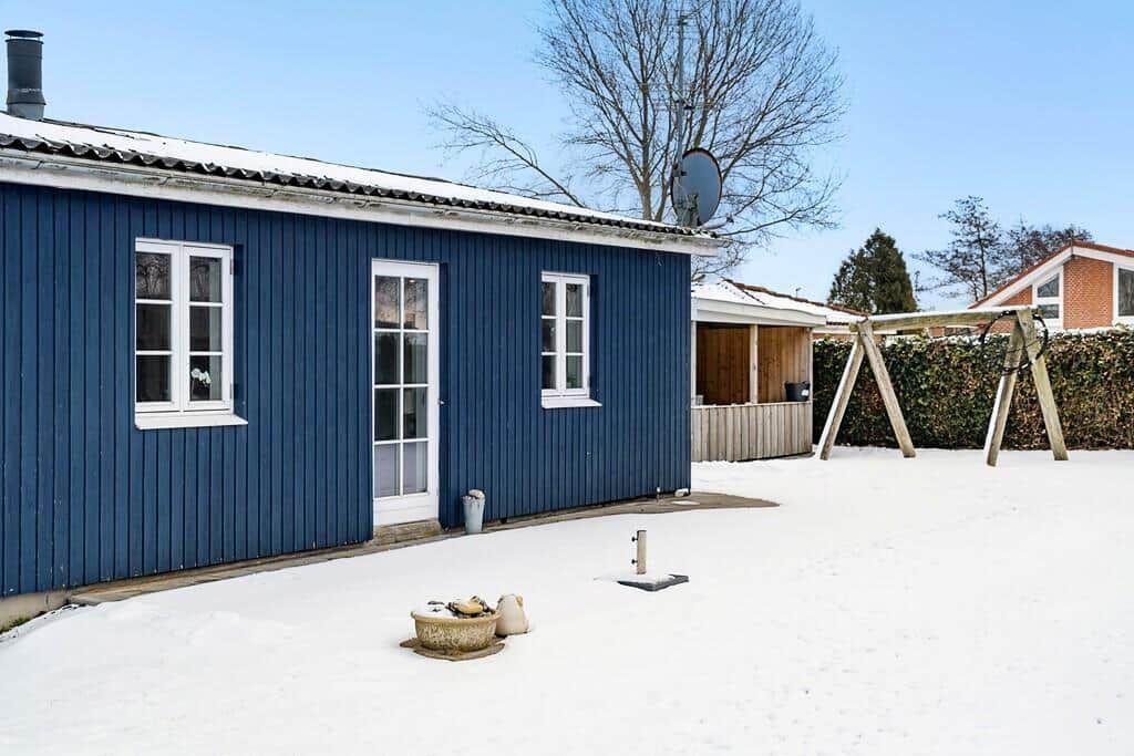 Blue-painted house with snow-covered garden and playground