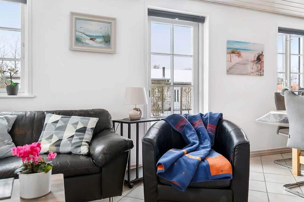 Living room with leather sofa, armchair, and windows. Wall art shows beach.