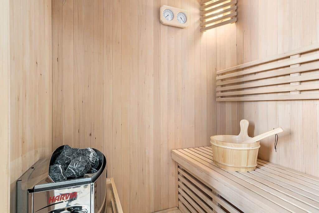 Sauna with wooden bench, wooden bucket, and thermostat on the wall.