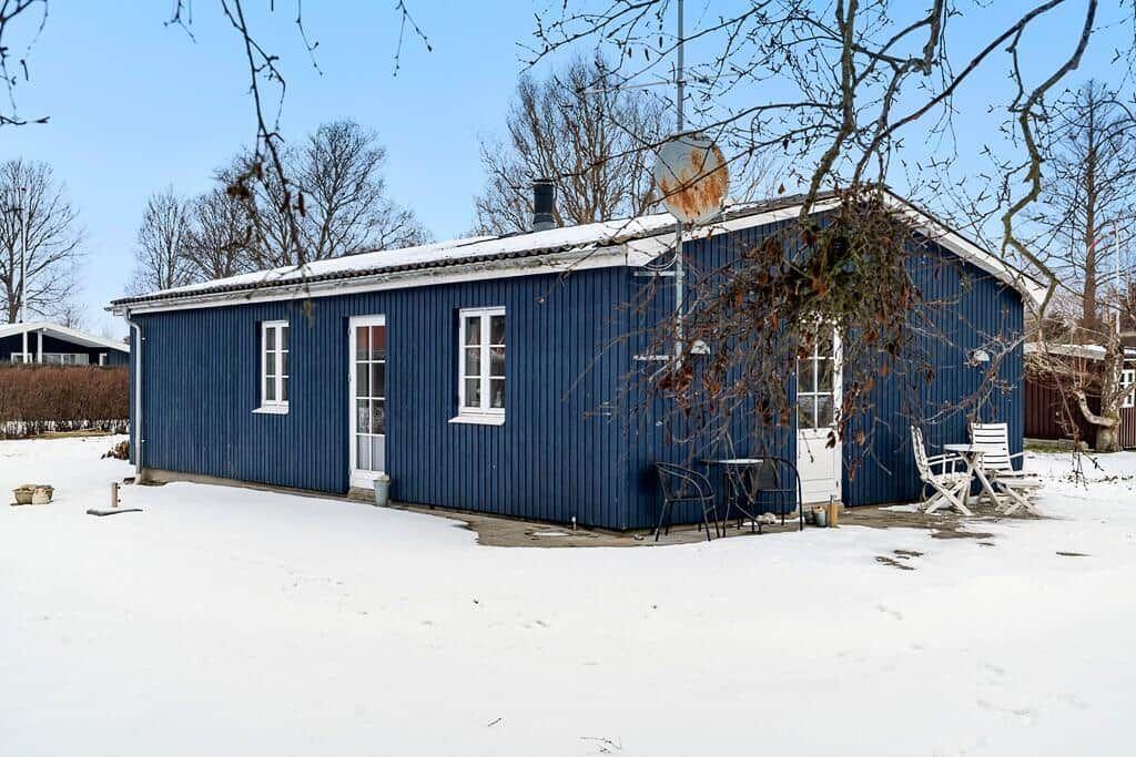 Blue wooden house with white door and windows. Snow covers the ground around the house.
