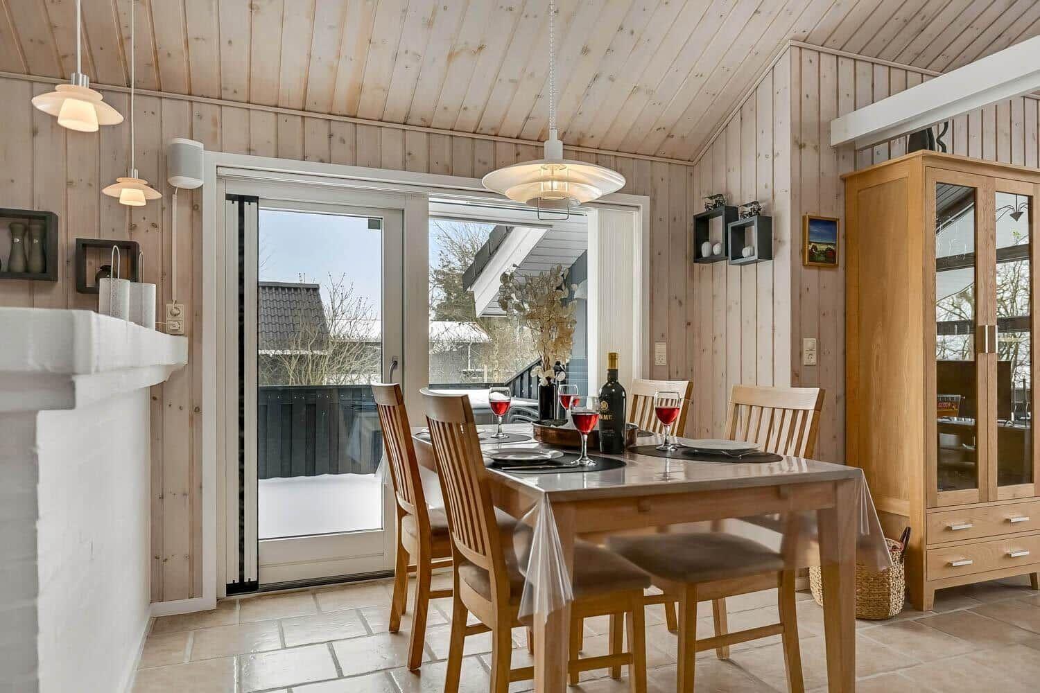 Esszimmer mit Holztisch, Stühlen und Blick auf Balkon. Holzwände und Decke.