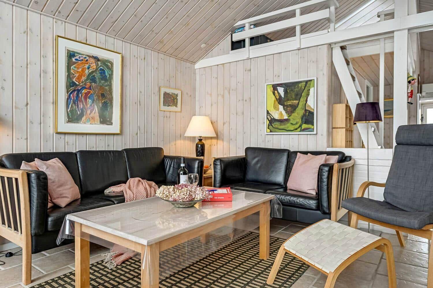 Wohnzimmer mit zwei schwarzen Sofas, Holztisch und Gemälden an den Wänden.