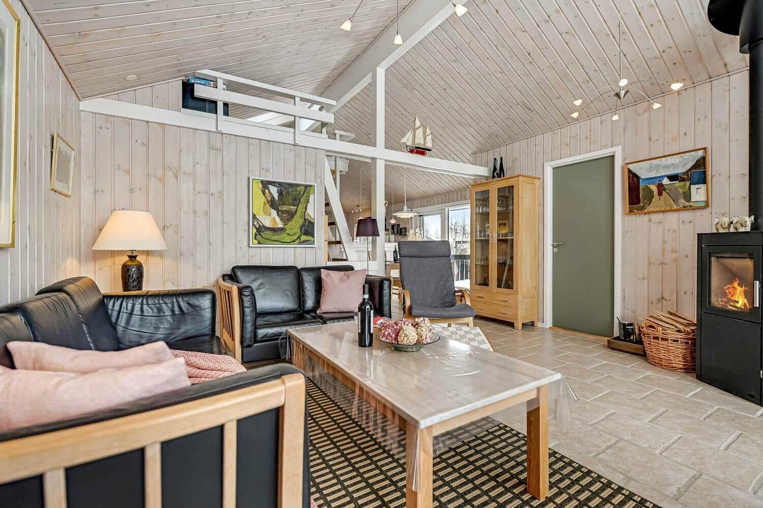Wohnzimmer mit Sofa, Couchtisch und Kaminofen. Holzwände und -decke. Treppenhaus im Hintergrund.