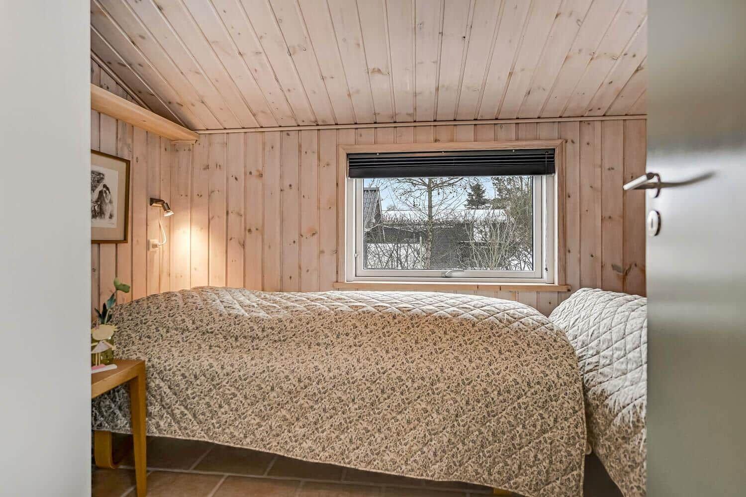 Schlafzimmer mit Holzwand, Bett und Fenster zum Außenbereich.